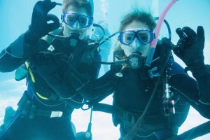 friends-scuba-training-submerged-swimming-pool-looking-camera