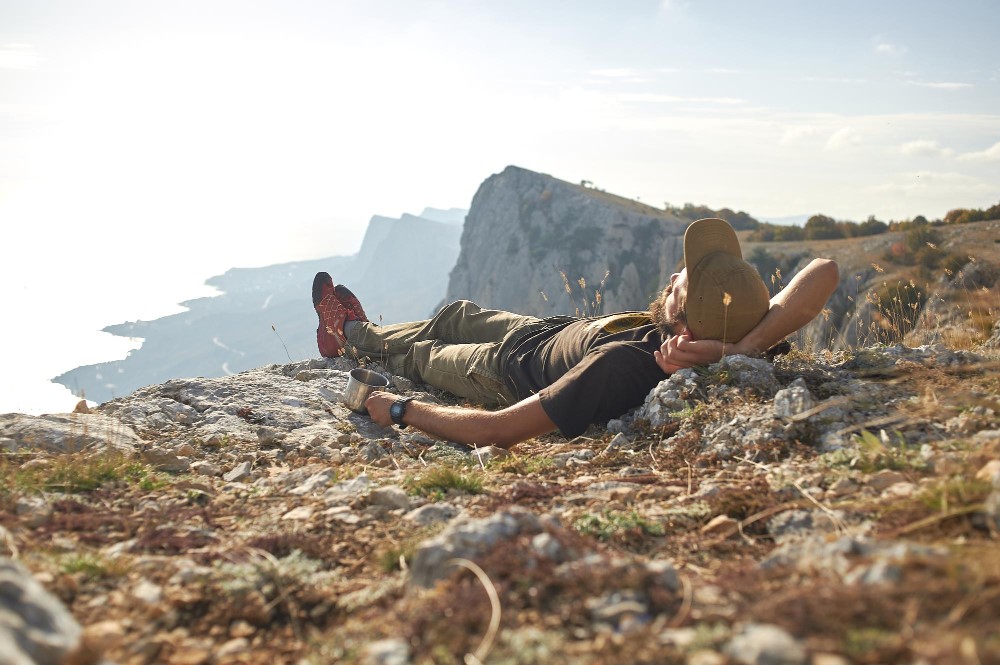 traveler-rests-lying-top-mountain-rays-setting-sun